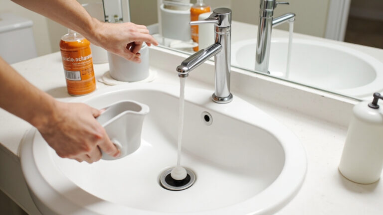 "Hands using a plunger to fix a slow-draining bathroom sink with baking soda and vinegar beside the drain"