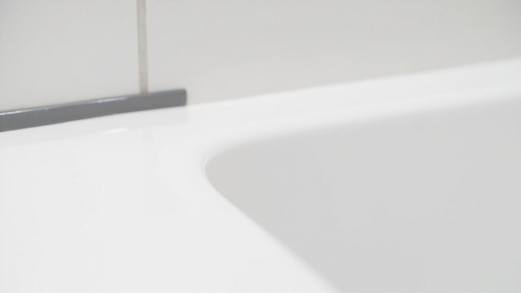 "Smooth grey silicone caulk bead sealing the gap between a white bathtub and tile wall in a clean bathroom"
