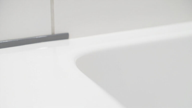 "Smooth grey silicone caulk bead sealing the gap between a white bathtub and tile wall in a clean bathroom"