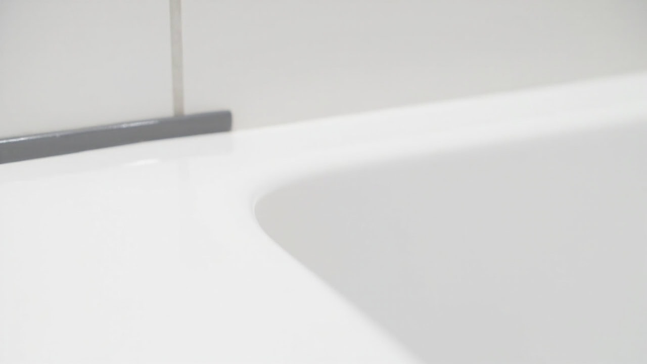 "Smooth grey silicone caulk bead sealing the gap between a white bathtub and tile wall in a clean bathroom"