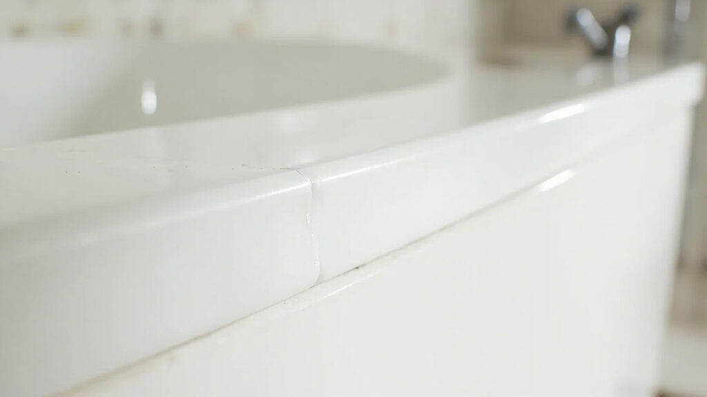 "Fresh silicone caulk seal along bathtub edge with tiled wall background"