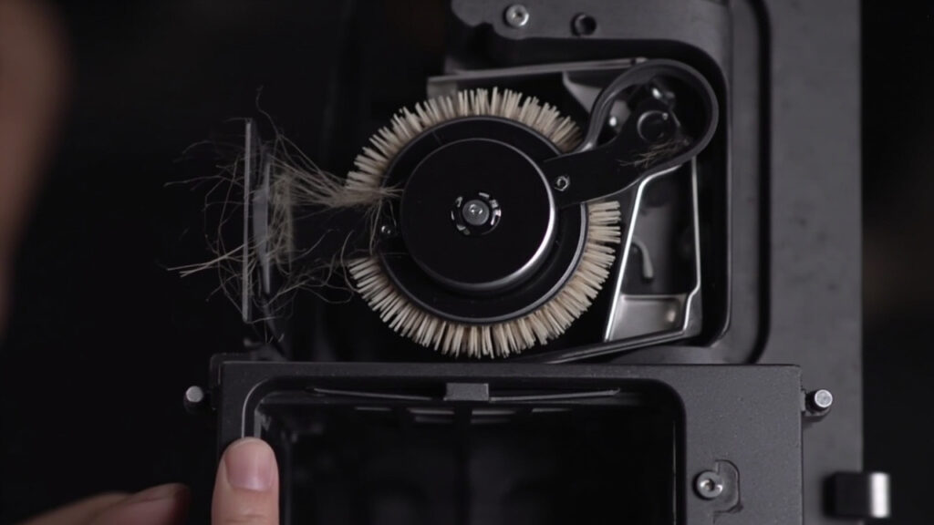 "Vacuum brush roll compartment showing belt drive mechanism and tangled hair debris around axle"