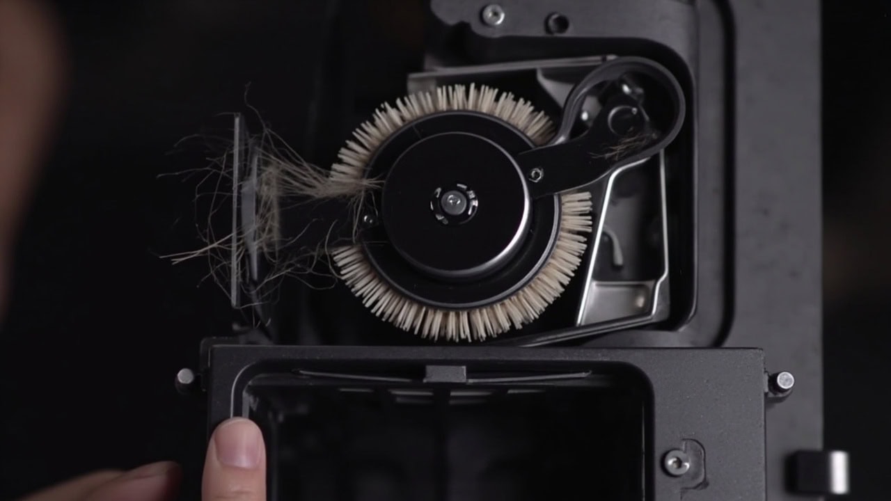"Vacuum brush roll compartment showing belt drive mechanism and tangled hair debris around axle"